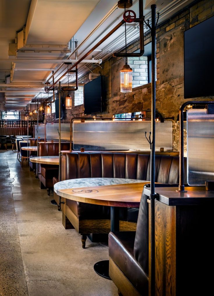 an empty restaurant with wooden benches and tables in the foreground, along with televisions on the wall