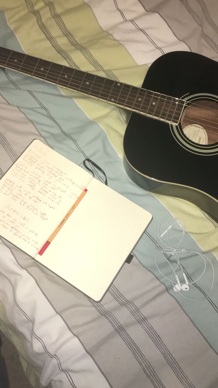 a guitar and notepad sitting on top of a bed