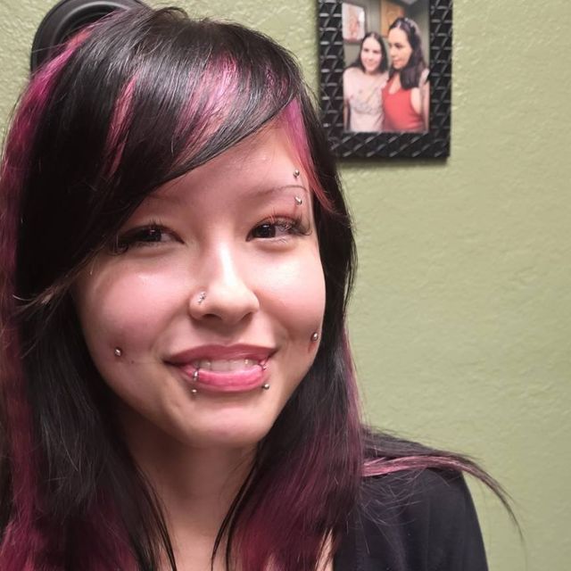 a woman with pink hair and piercings smiling at the camera