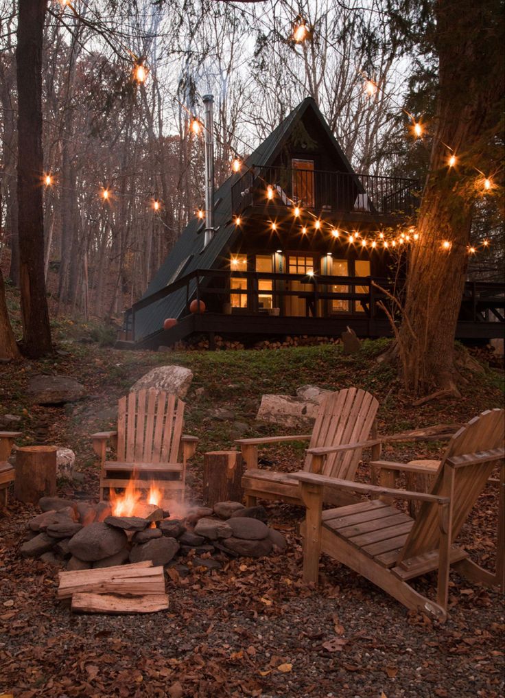 an outdoor fire pit with chairs around it and string lights strung over the back porch