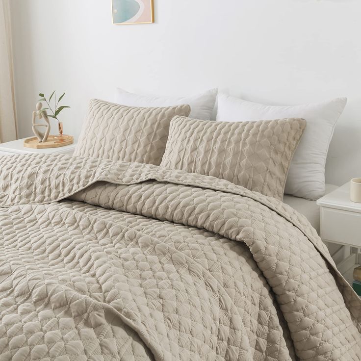 a bed covered in a beige quilt and pillows