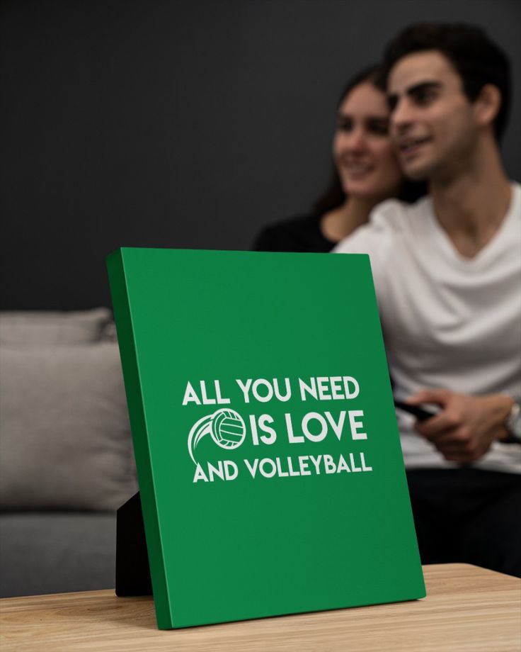 two people sitting on a couch with a green sign that says all you need is love and volleyball