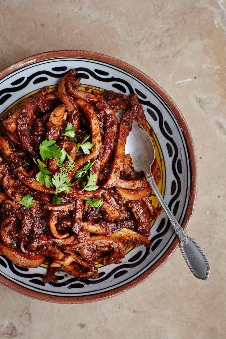 a bowl filled with meat and garnish on top of a table next to a spoon