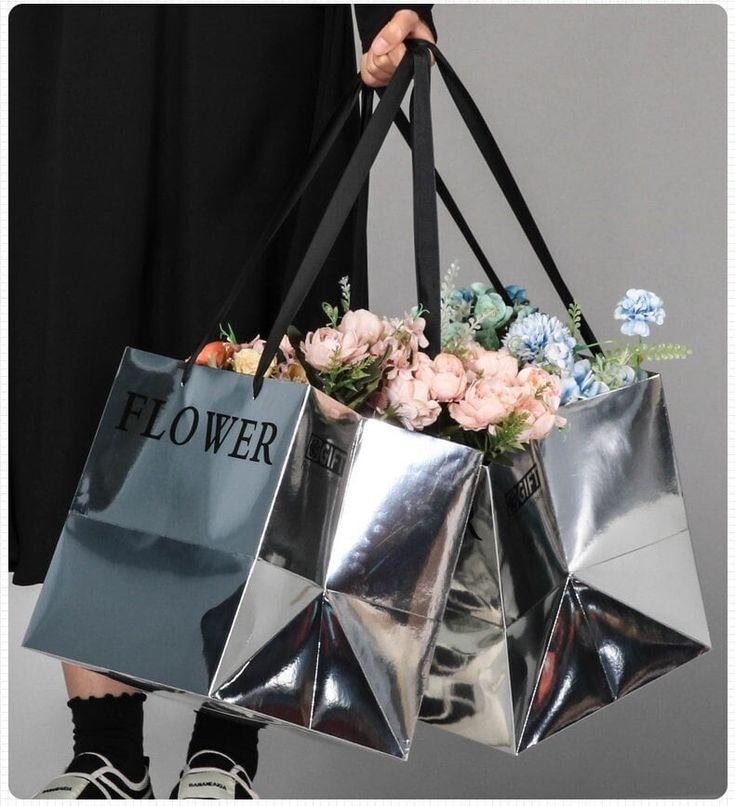 a woman holding two shopping bags with flowers in them