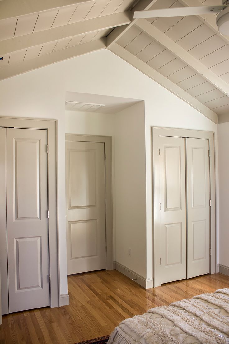 an empty bedroom with white walls and wooden floors is pictured in this image, there are three doors on each side of the room