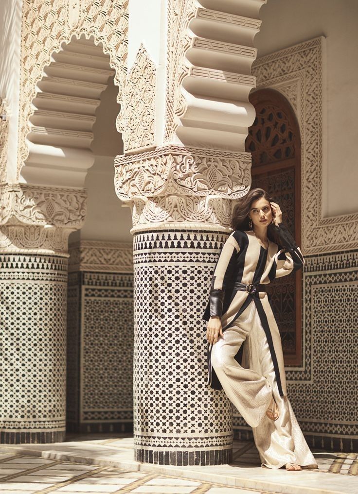 a woman standing next to a white and black wall in a room with arches on the walls