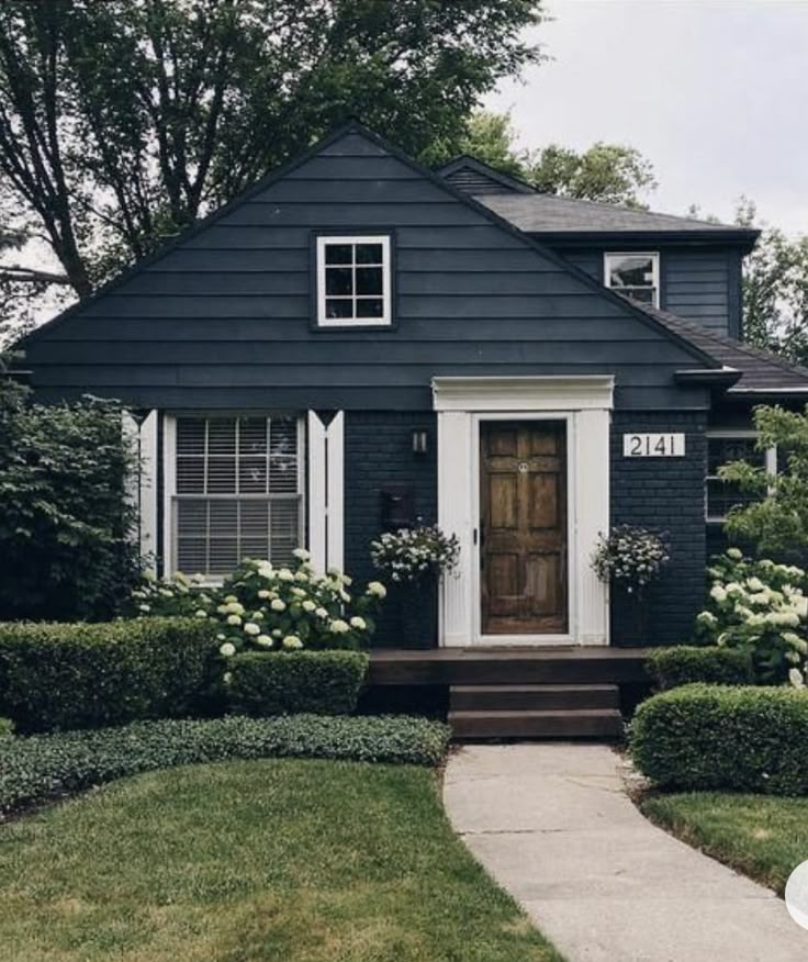 a blue house with white trim and flowers on the front door is surrounded by hedges