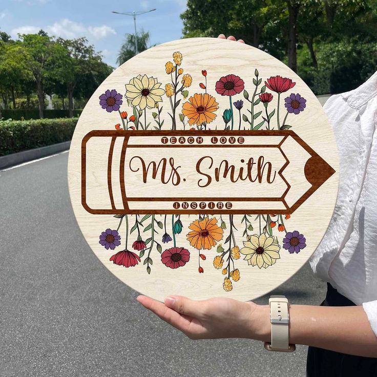 a woman holding up a wooden sign that says, mrs smith with flowers on it