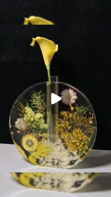 a vase filled with flowers and plants on top of a white table next to a black wall