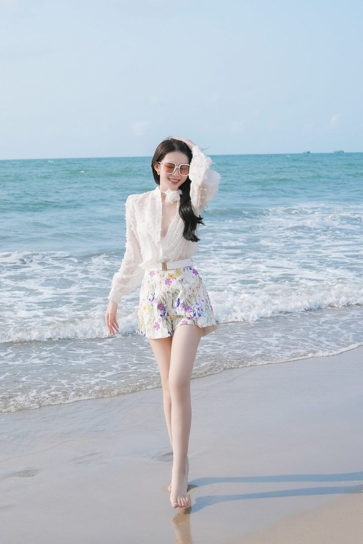 a woman is walking on the beach with her hand in her hair and wearing sunglasses