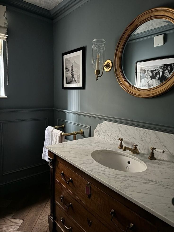 a bathroom with blue walls and marble counter top, gold framed mirror above the sink