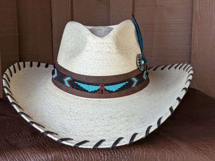 The Maverick starts with a Mexican soft palm leaf hat body that has a 3 3/4" brim and 5 1/4" crown. Hand laced in chocolate brown leather lace. The beaded hatband has a Thunderbird pattern and then mounted on distressed leather. The back of the band has a deer antler bead for accent. Starburst turquoise Concho and deep blue/green decorative feather completes the hat. All hats are made to order. Allow up to 4 weeks for your hat to ship. Brown Toquilla Straw Hat Bands For Ranch, Western Style Brown Panama Hat With Flat Crown, Brown Toquilla Straw Hat Band For Western-themed Events, Western Brown Panama Hat With Flat Crown, Brown High Crown Hat For Rodeo, Brown High Crown Country Hat, High Crown Brown Country Hat, Handmade Fitted Brown Hat Bands, Western Panama Hat With Flat Crown For Country Events