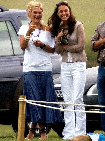 two women standing next to each other in front of a dog on a field with cars behind them