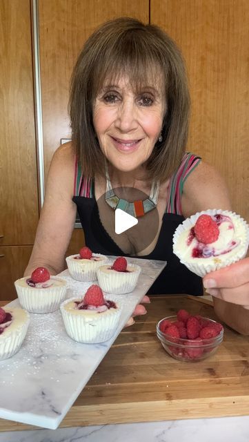 a woman sitting at a table with cupcakes and raspberries