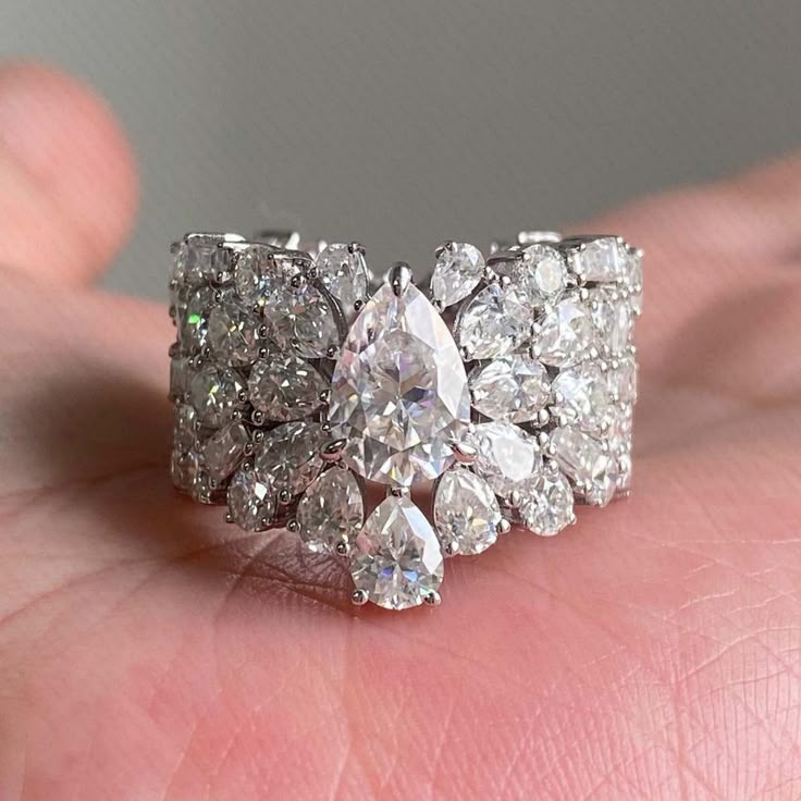 a close up of a person holding a ring on their hand with diamonds in it