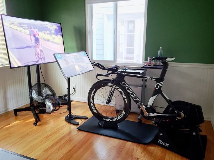 there is a bike that is on the floor in front of two monitors and a fan