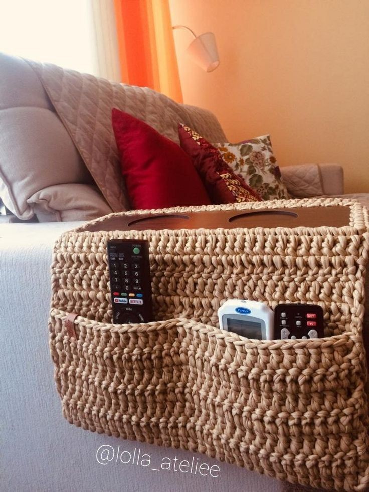 a couch with two remotes and a basket on the back that is attached to it