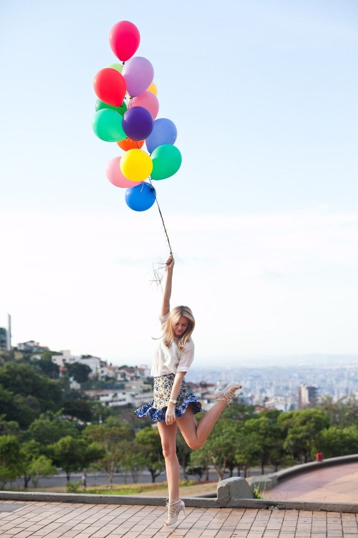 a woman is holding balloons in the air while standing on a brick walkway with her legs up