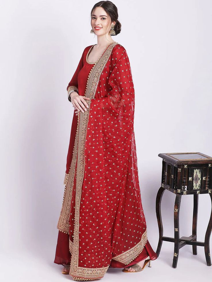 Experience exclusive, elevated luxury wearing our maroon silk palazzo set with organza dupatta. Adorned with intricate zari and sequin work, our regal piece captures timeless sophistication with its rich hues, silken textures, and ornate detailing. Exuding an aura of refined elegance, treat yourself to an extraordinary yet understated look. No. of pieces - 3 piece set. Fabric - Silk and Organza. Color - Maroon. Kurta Length - 42 inches. Washing Instructions - Dry Clean. Red Anarkali Set With Sheer Dupatta For Eid, Eid Red Anarkali Set With Sheer Dupatta, Elegant Red Salwar Kameez With Cutdana, Eid Raw Silk Palazzo Set With Dori Work, Floor-length Chanderi Sharara With Dupatta, Eid Palazzo Set With Dori Work In Raw Silk, Raw Silk Palazzo Set With Sheer Dupatta For Navratri, Festive Chanderi Palazzo Set With Sheer Dupatta, Diwali Dola Silk Palazzo Set With Dori Work