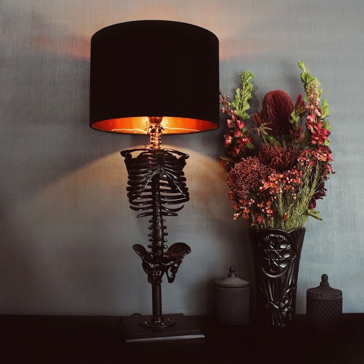 a skeleton lamp next to a vase with flowers in it on a black table top