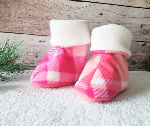 pink and white checkered baby booties sitting next to a pine tree