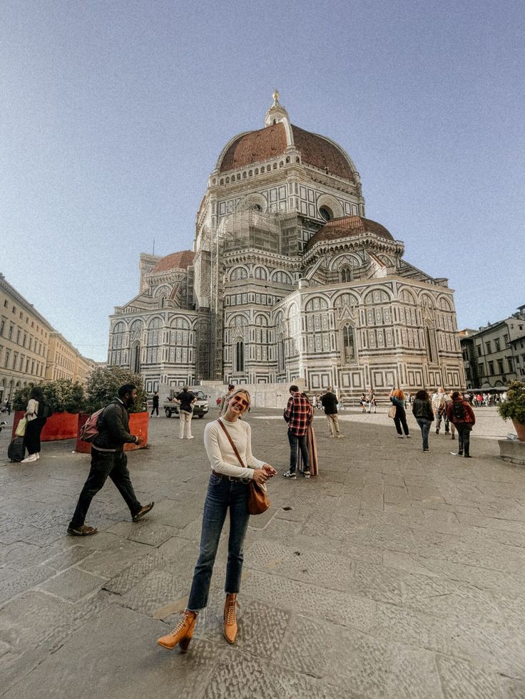 a woman standing in front of a large building with people walking around it and onlookers