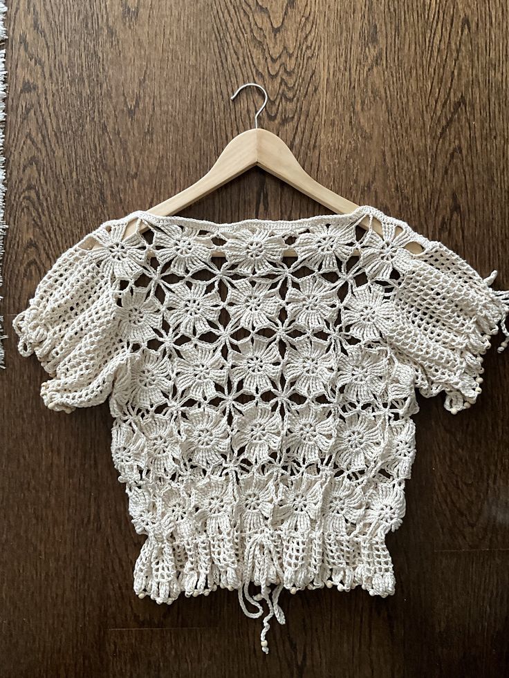 a white crocheted top hanging on a wooden wall