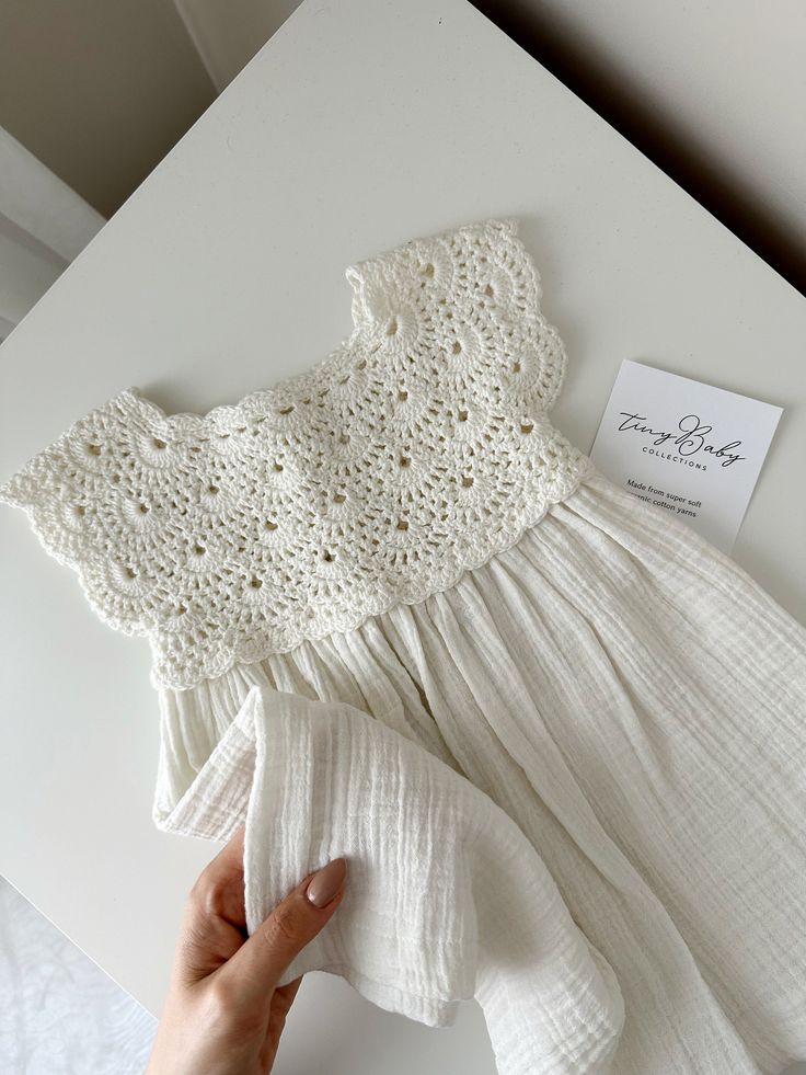 a hand is holding a white piece of cloth next to a crocheted dress