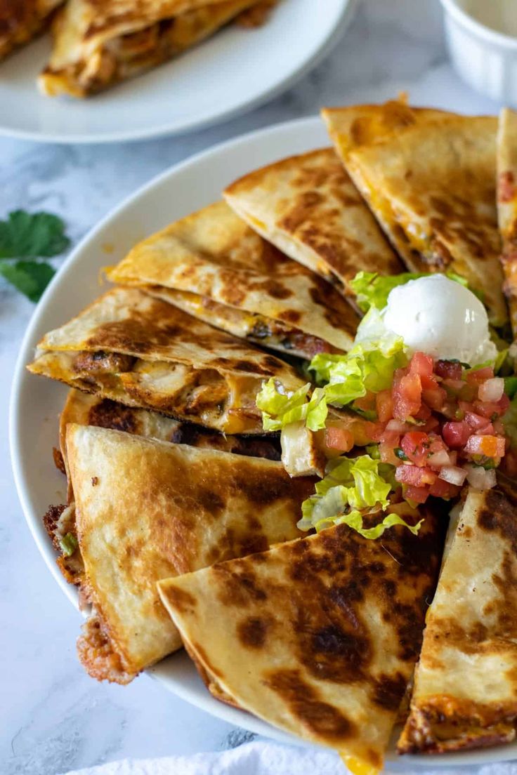 several quesadillas are arranged on a plate with salsa and sour cream in the middle