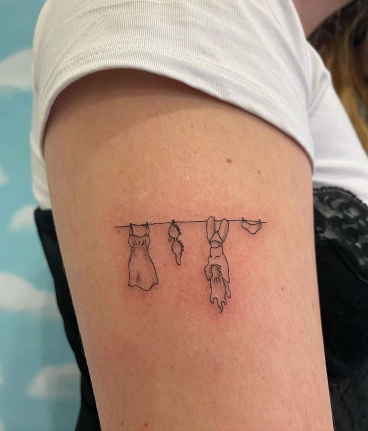 a woman's arm with three clothes hanging on a line tattooed to the side