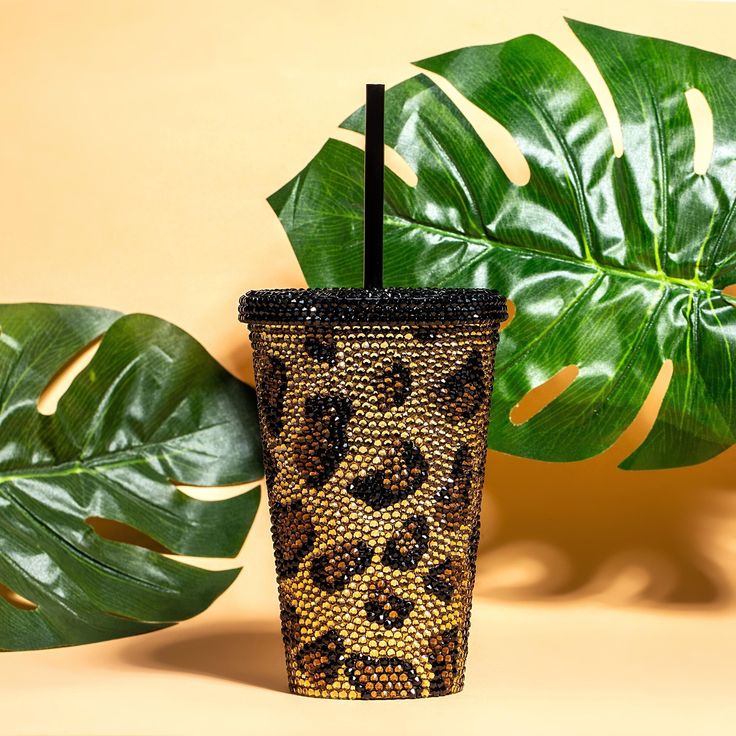 a cup with a straw in it sitting next to a green plant and a banana leaf