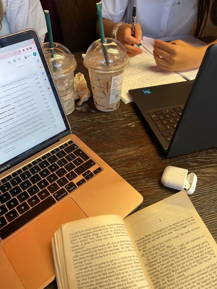 an open laptop computer sitting on top of a wooden table next to a book and cup