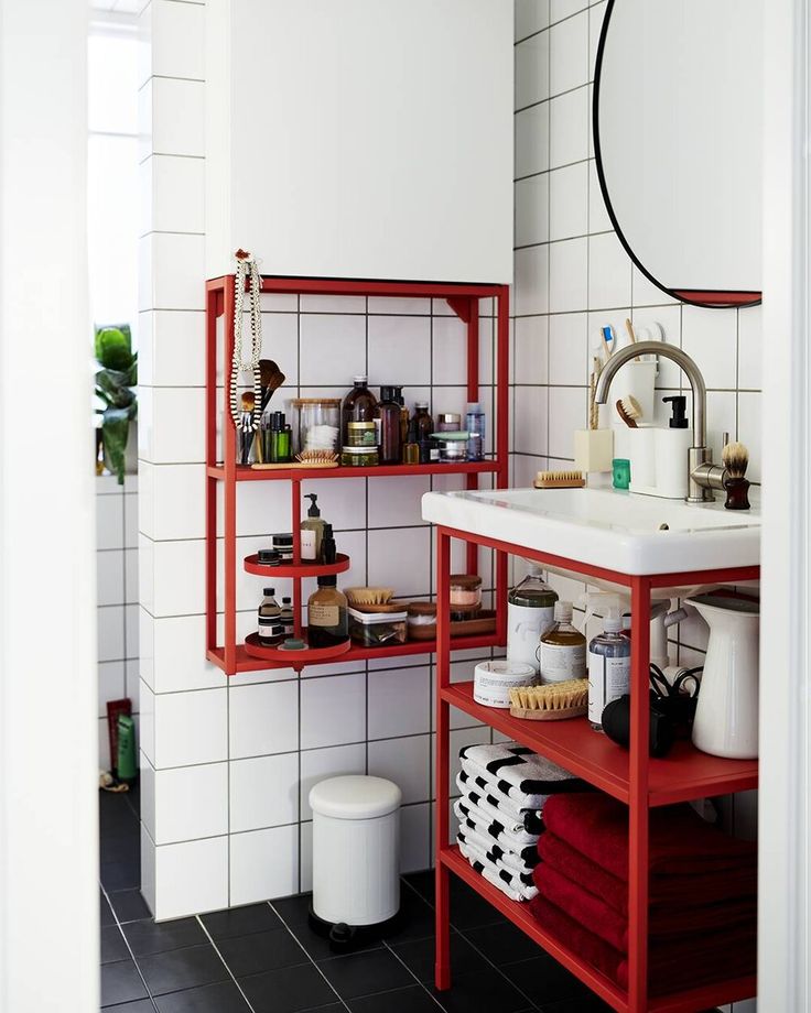 a bathroom with white tile and red shelving unit next to the sink in it