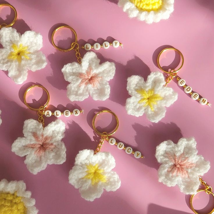 crocheted keychains are arranged on a pink surface with white and yellow flowers