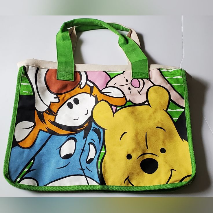 a winnie the pooh tote bag on a white surface with green handles and straps