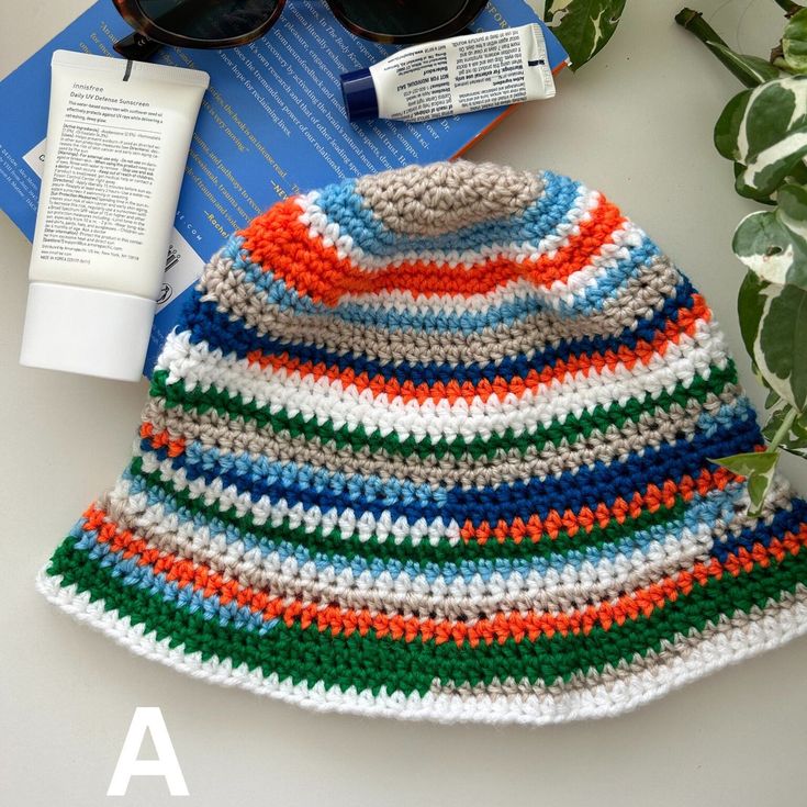 a crocheted hat and sunglasses on top of a book next to a plant