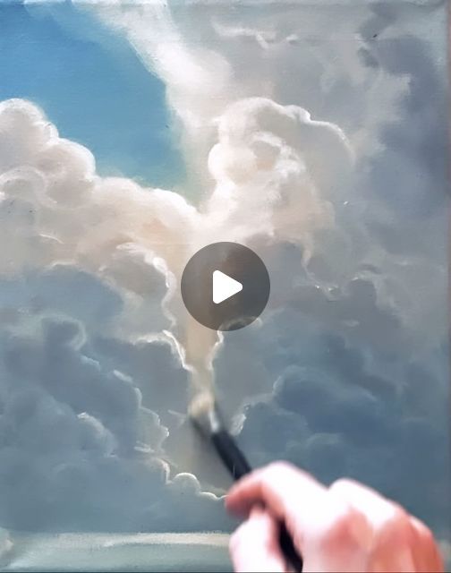 a person holding a paintbrush in their left hand and painting clouds on the right