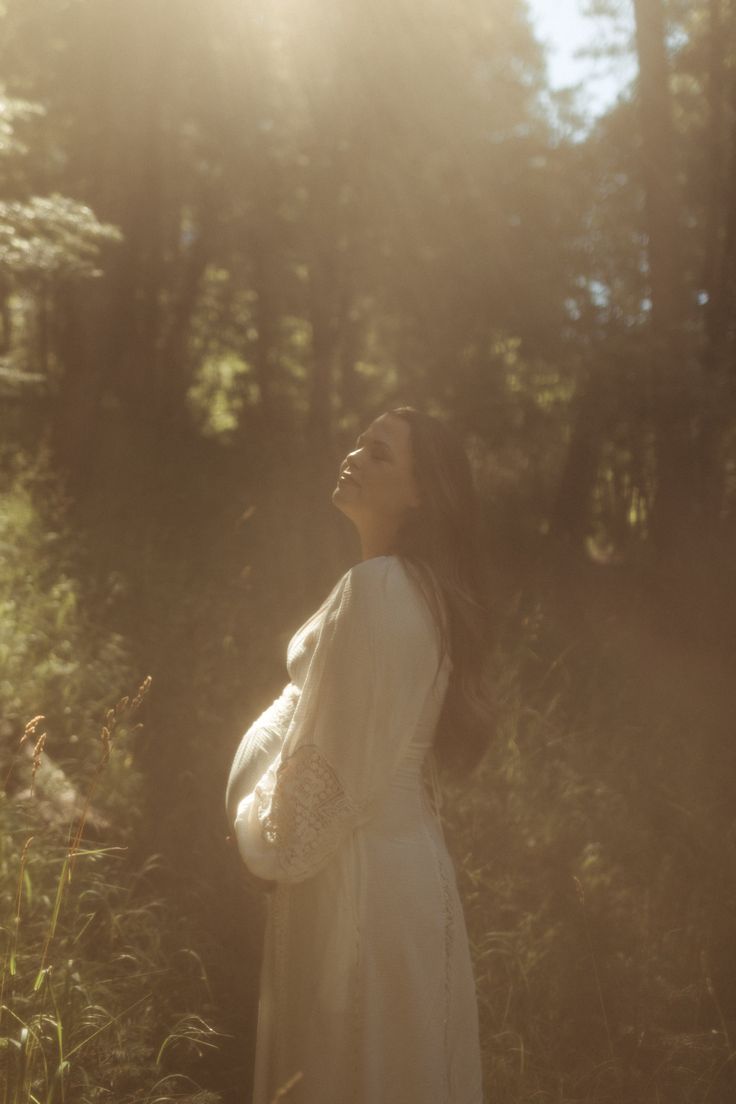 a pregnant woman standing in the woods with her eyes closed and looking up at the sky