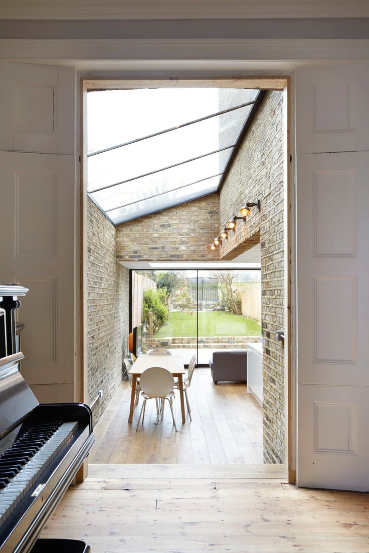 an open door leading to a dining room with a piano in the foreground and a large window on the far wall