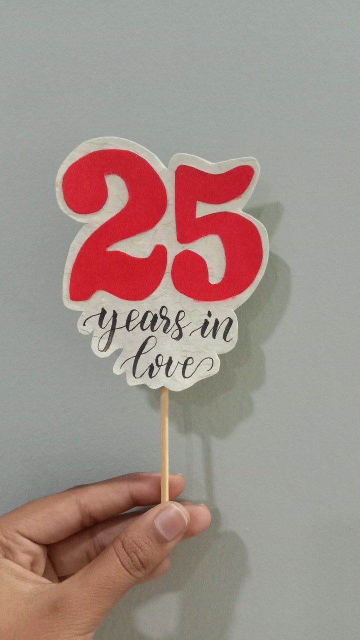 a hand holding a cake topper that says 25 years in love