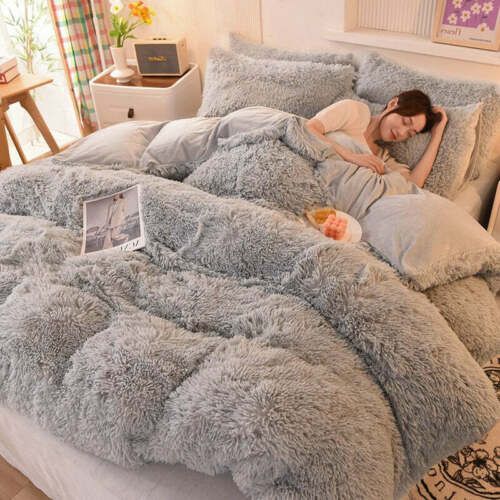 a woman laying in bed on top of a fluffy gray comforter and pillow set