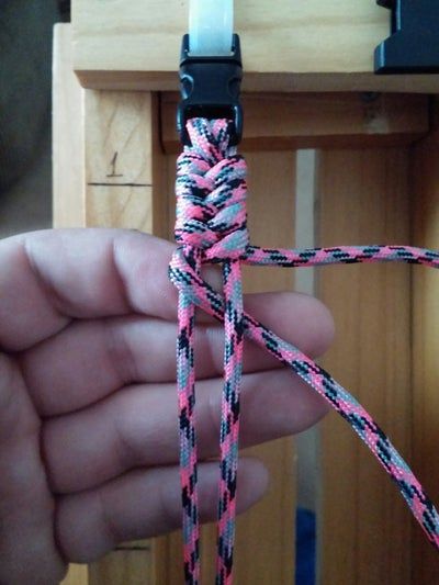 a hand holding a pink and black rope in front of a wooden cabinet with drawers