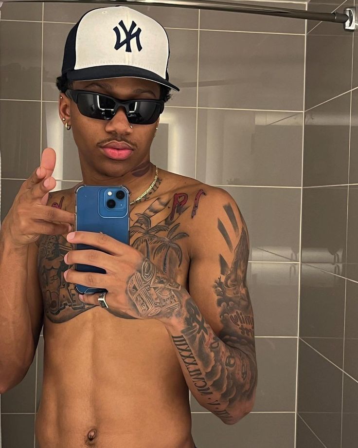 a shirtless man taking a selfie in the bathroom with his cell phone and sunglasses on