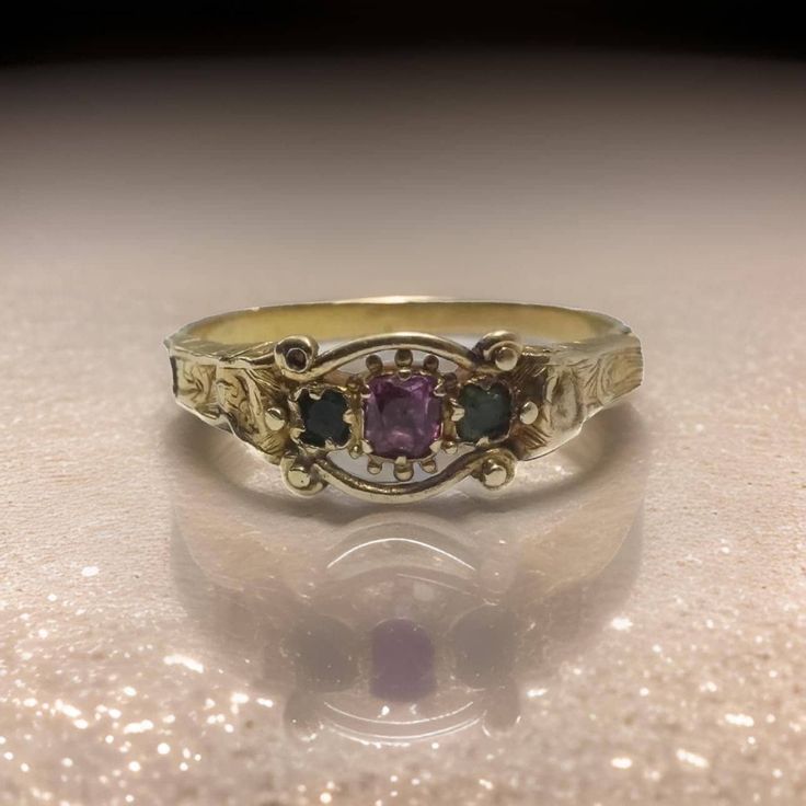 Immerse yourself in the grandeur of the Victorian era with this exceptional antique ring, a treasure from the mid-19th century (tests thereabouts). Crafted with precision, this ring is made from solid 18 carat gold, tested to near perfection, and exudes a timeless elegance that is both rare and captivating. At the heart of this royal piece lies a luminous, foiled natural ruby, its vibrant red hue symbolizing passion and nobility. This stunning gemstone is gracefully flanked by two natural emeral Green And Gold Promise Ring, Unique Vintage Engagement Rings Antiques, Vintage Stone Ring, Vintage Floral Ring, Vintage Wedding Rings Antique Silver, Antique Oval Multi-stone Ring, Ceremonial Yellow Gold Emerald Heirloom Ring, Ceremonial Heirloom Yellow Gold Emerald Ring, Victorian Engraved Yellow Gold Ring For Ceremonial Occasion