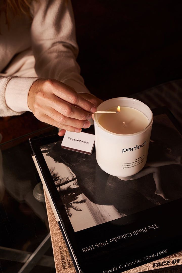 a person holding a lit candle over a cup on top of a book and magazine