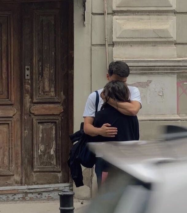 two people hugging each other in front of a building with an orange heart on it