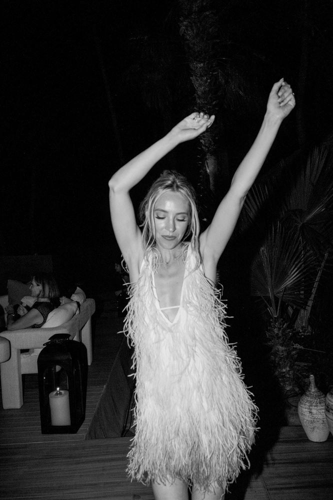 a woman in a feathered dress is holding her arms above her head and looking at the camera