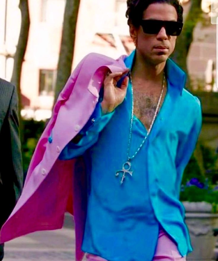 a man in blue shirt and pink pants walking down the street with his jacket open