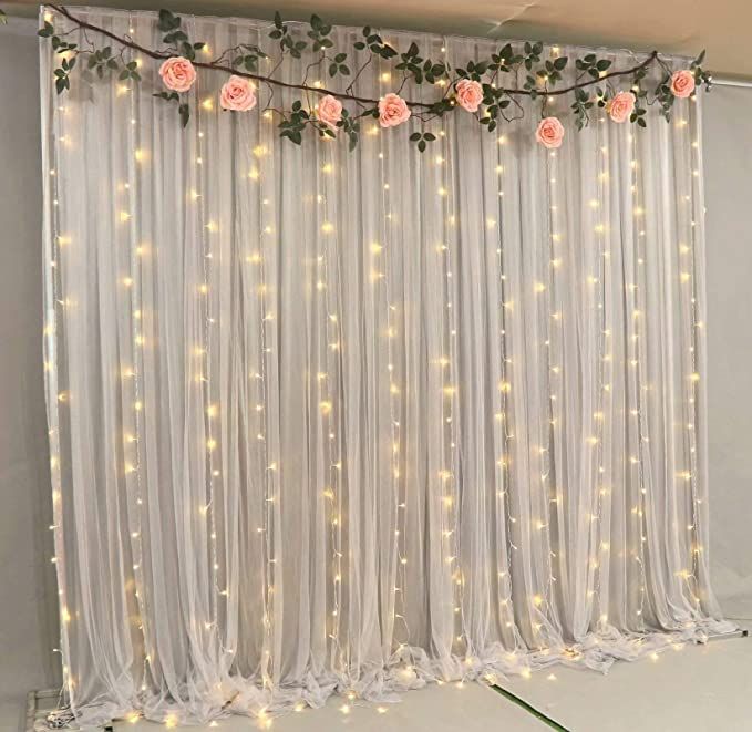 the room is decorated with white curtains and pink flowers on them, along with fairy lights