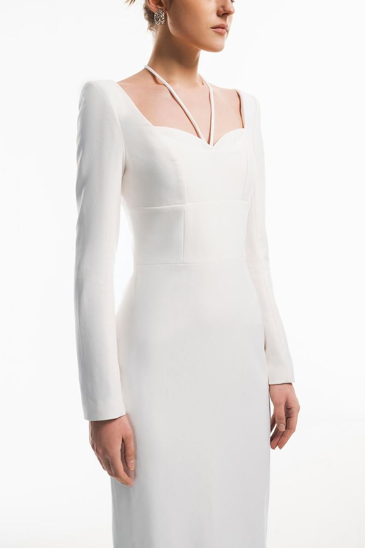 a woman wearing a white dress with long sleeves and an open neckline, standing in front of a white background